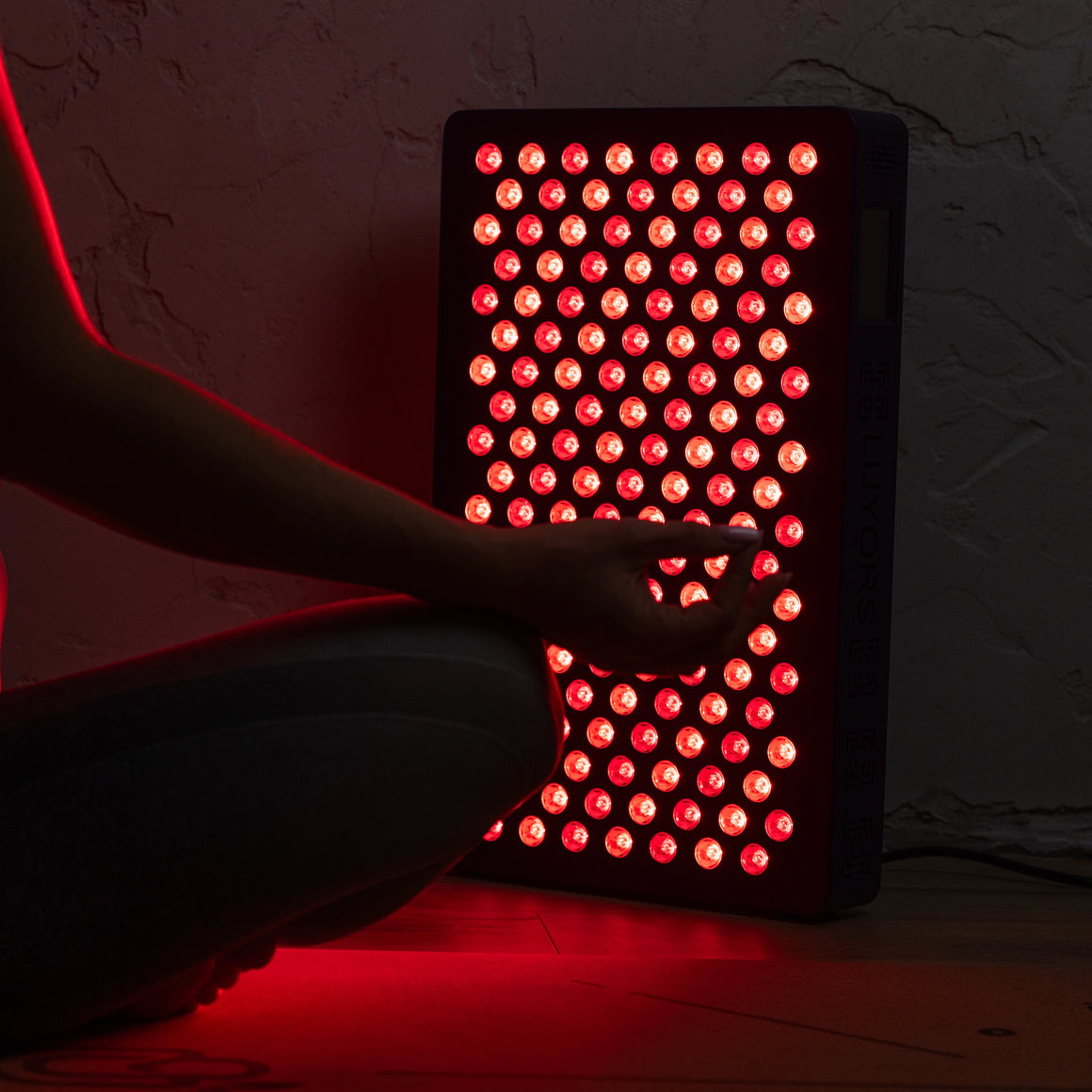 Close-up-of-the-6-Wavelength-LED-Therapy-Panel's-red-and-near-infrared-LEDs-glowing-as-a-seated-person-reaches-toward-it