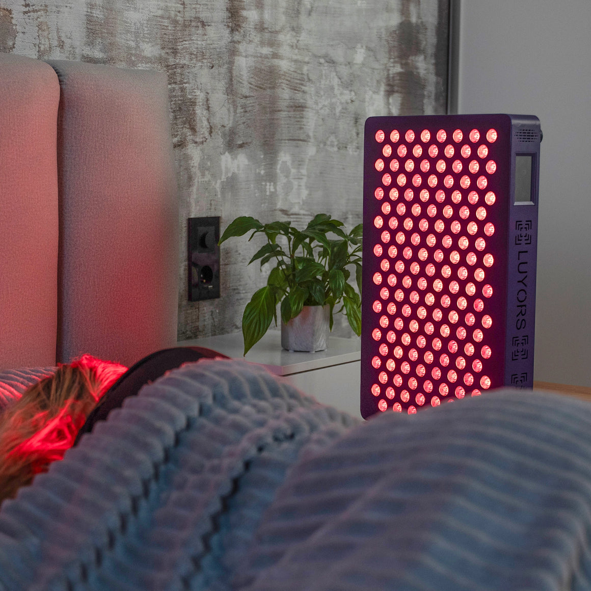6-Wavelength-LED-Therapy-Panel-glowing-red-on-a-bedside-table-beside-a-person-resting-in-bed
