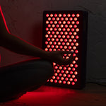 Close-up-of-the-6-Wavelength-LED-Therapy-Panel's-red-and-near-infrared-LEDs-glowing-as-a-seated-person-reaches-toward-it