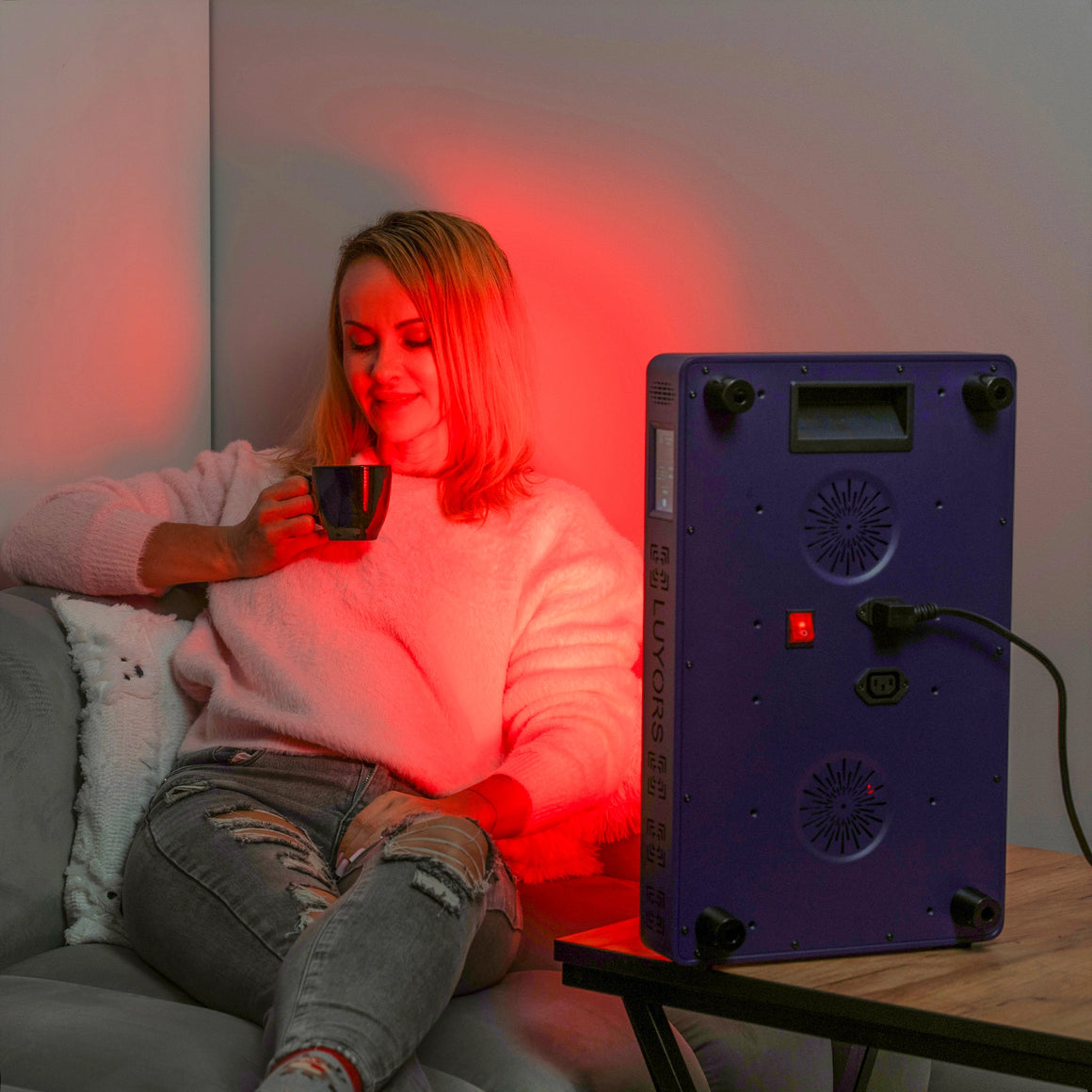 Woman-relaxing-with-coffee-beside-6-Wavelength-LED-Therapy-Panel-showing-back-controller,-cooling-fans-and-power-cord