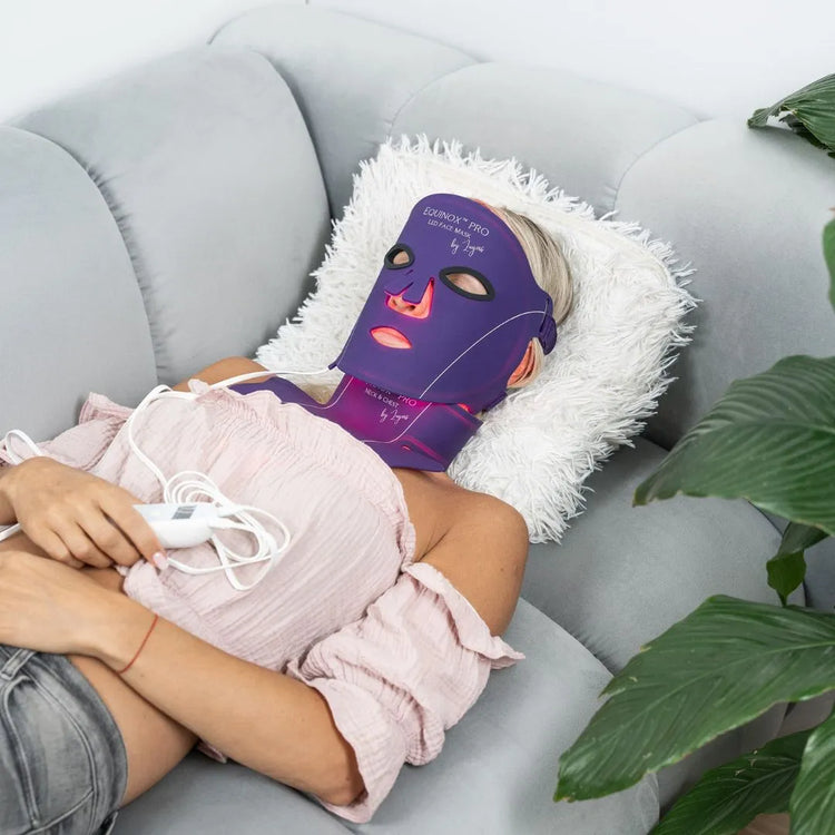 Woman lying down sleeping with Equinox Pro LED mask on face, neck and chest with warm glowing red light activated